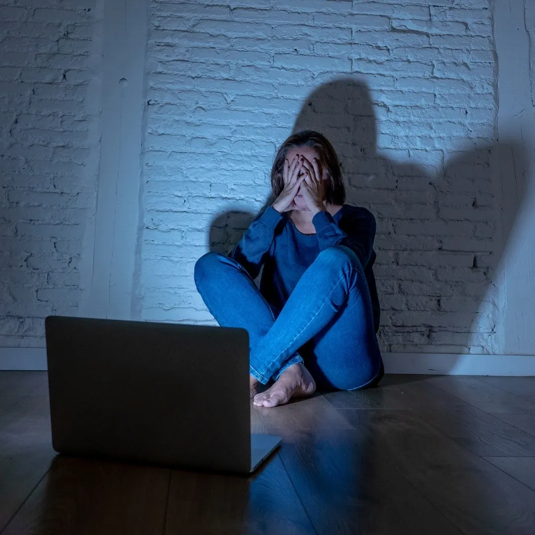 A woman sitting on the floor in front of a laptop.