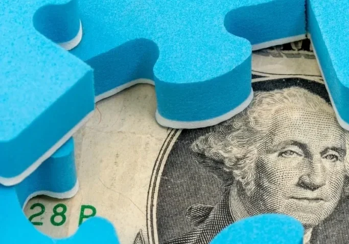 A close up of a dollar bill with blue puzzle pieces